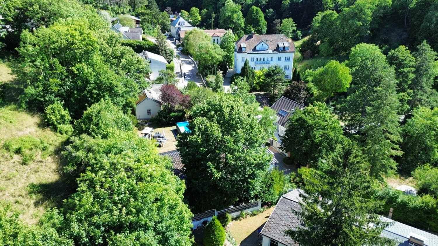 Luftaufnahme eines Wohngebiets in einem grünen Tal mit Häusern und einem kleinen Poolbereich.