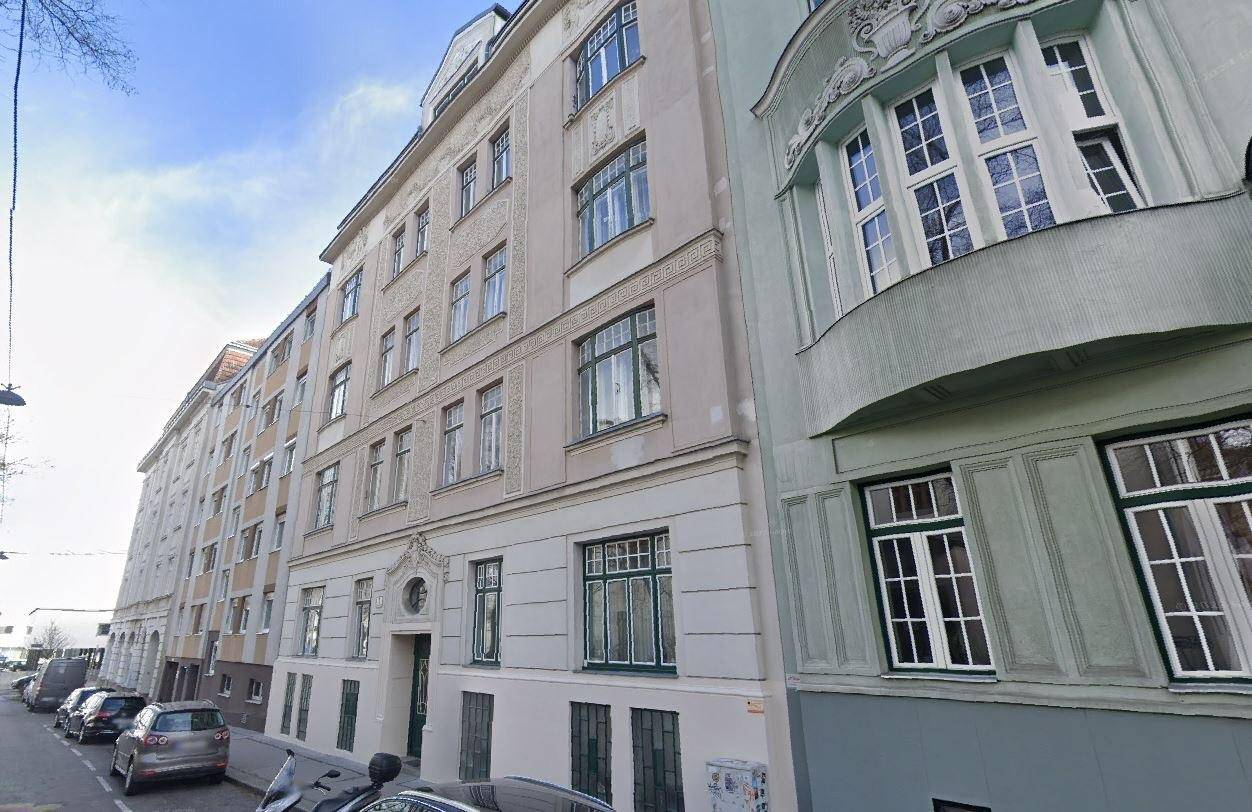 Fassade eines Mehrfamilienhauses mit klassischer Architektur und geparkten Autos auf der Straße.