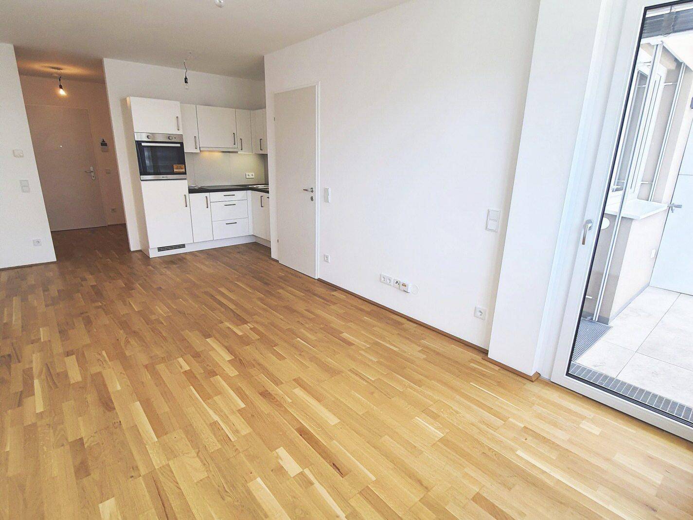 Offener Wohnbereich mit integrierter Küchenzeile, Parkettboden und direktem Zugang zum Balkon.