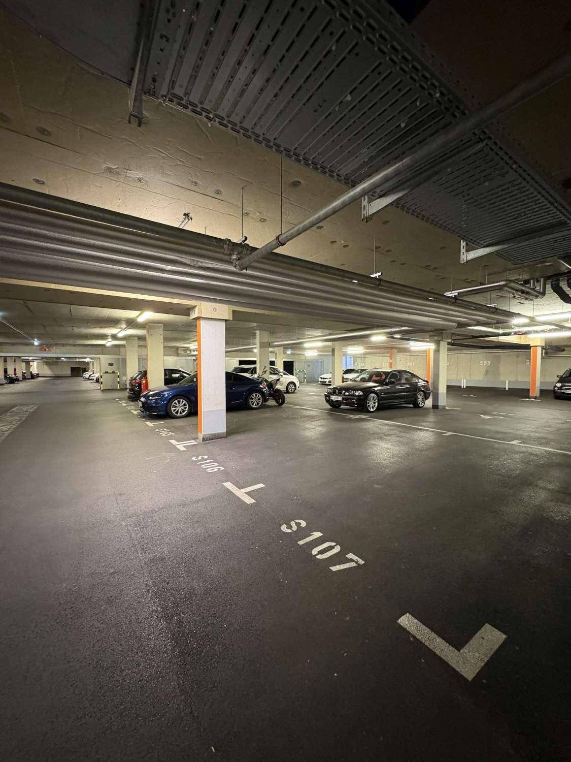 Tiefgarage mit nummerierten Stellplätzen und sichtbaren Rohren an der Decke.