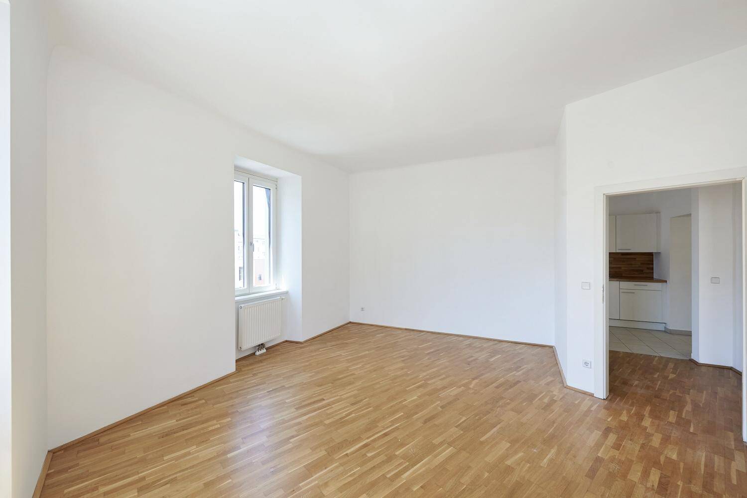 Heller Wohnraum mit Parkettboden und Zugang zu einem weiteren Zimmer, ideal für offenes Wohnen.
