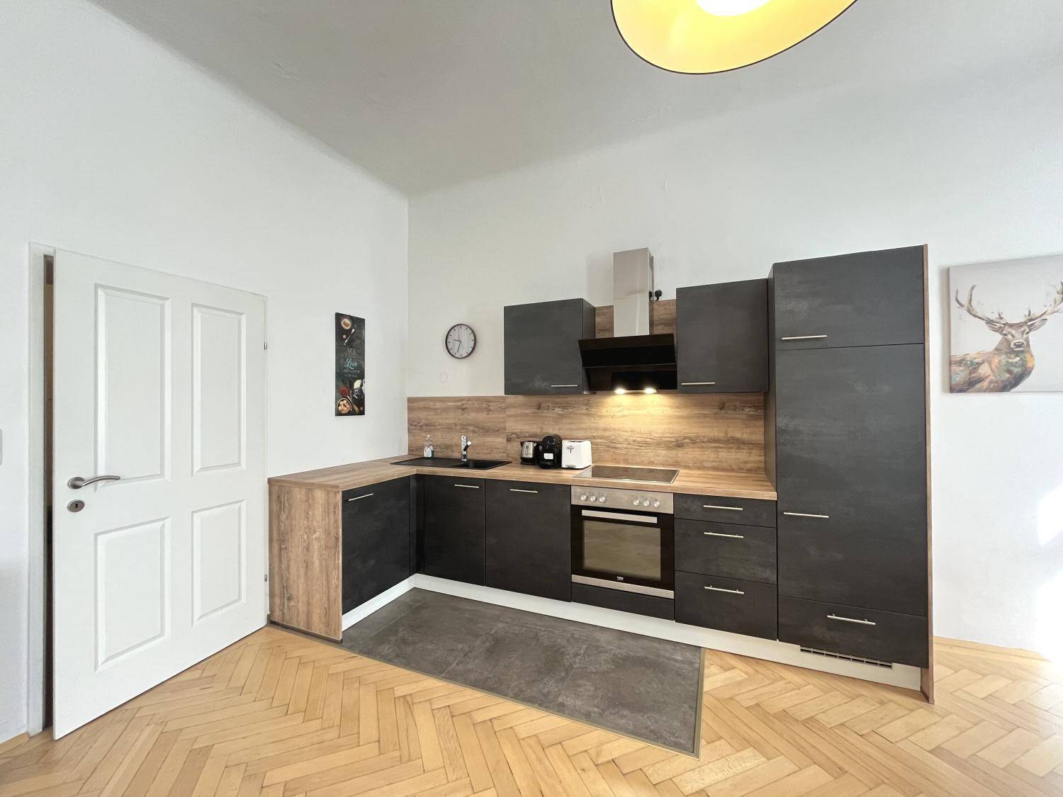Kompakte, moderne Einbauküche mit dunklen Fronten, Holzdetails und Parkettboden.