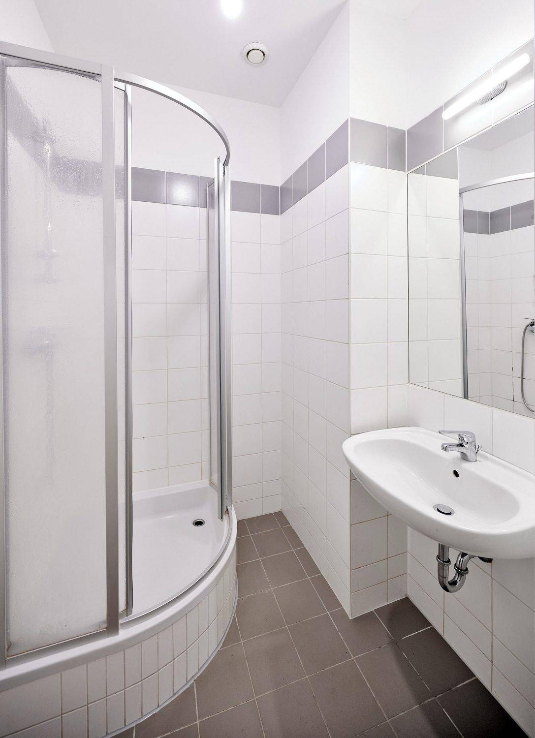 Modernes Badezimmer mit Duschkabine, Waschbecken und weißen Fliesen mit grauen Akzenten.