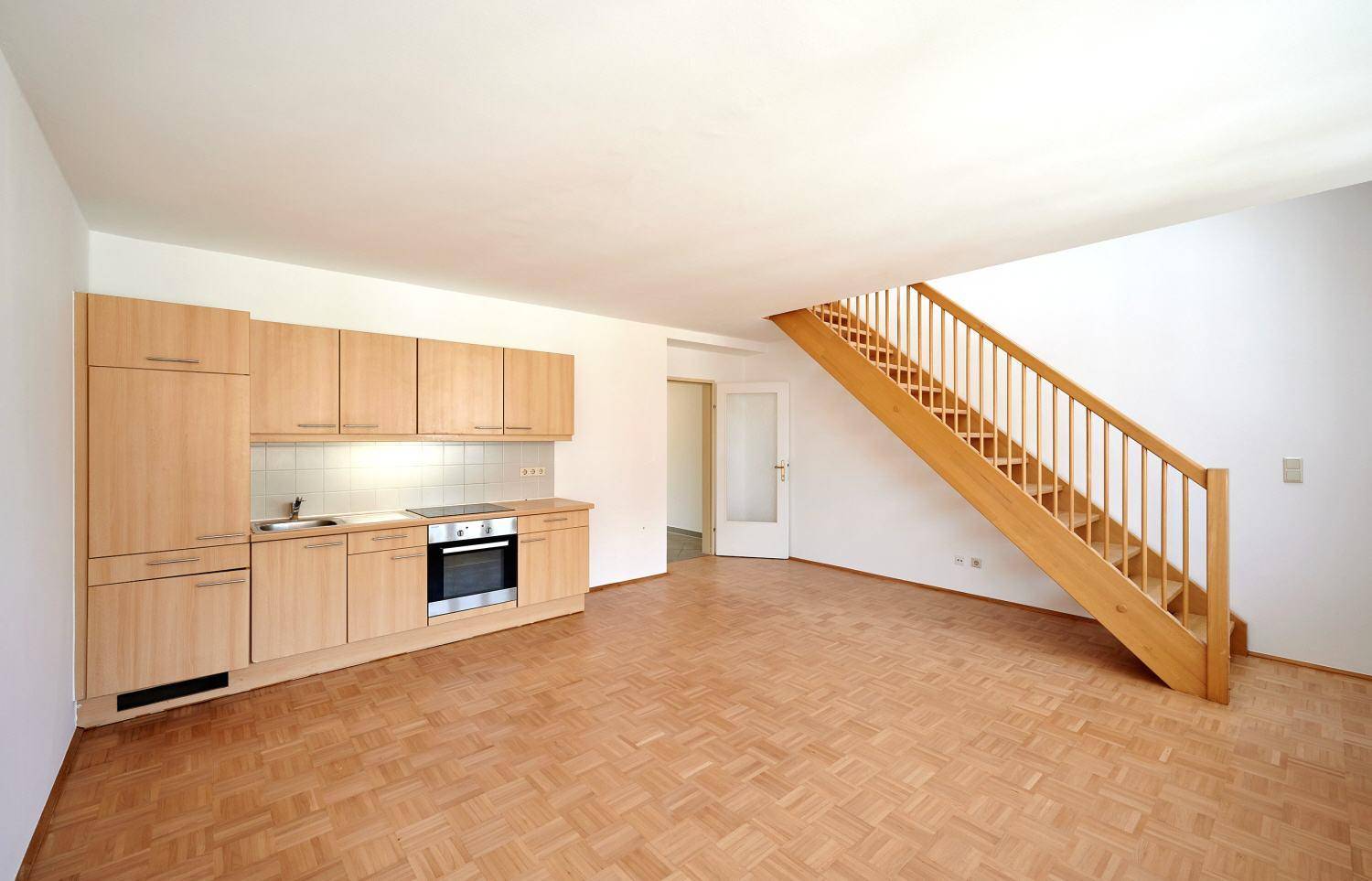 Offener Wohnbereich mit integrierter Küchenzeile und Holztreppe, ideal für modernes Wohnen.