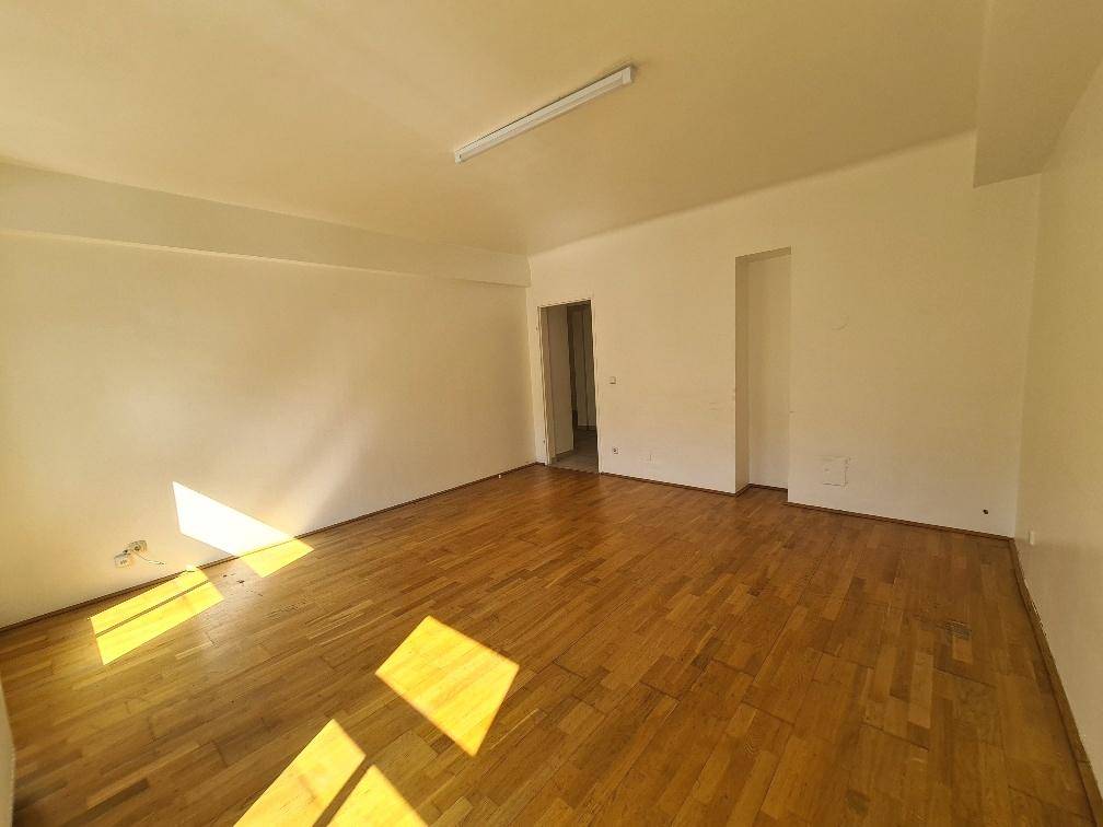 Leeres Zimmer mit glänzendem Parkettboden und einem Durchgang zu weiteren Räumen.
