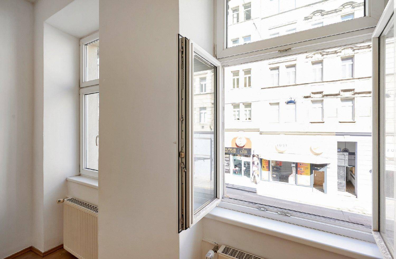 Blick aus dem Fenster auf die belebte Straße und gegenüberliegende Gebäude mit Geschäften.
