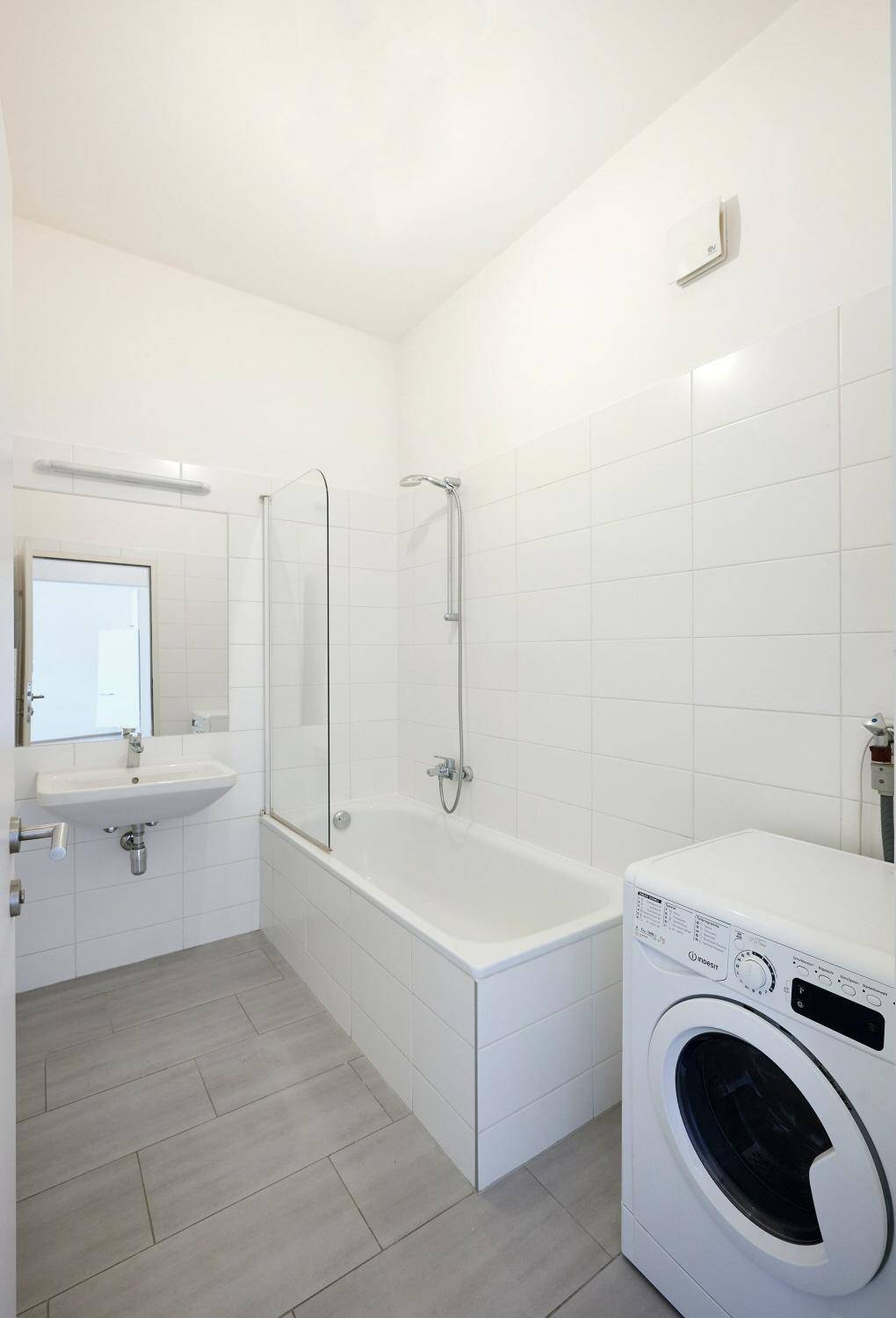 Modernes Badezimmer mit Badewanne, Waschbecken und Waschmaschine, komplett gefliest.
