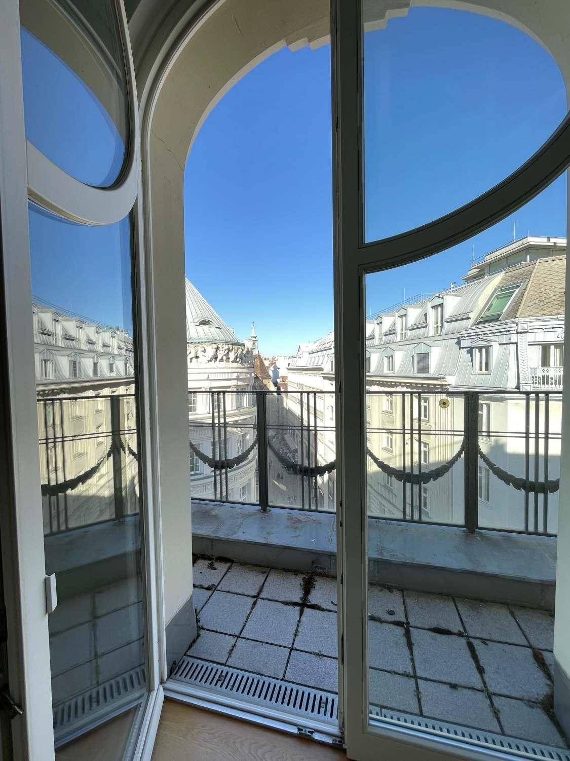 Blick durch große Fenstertüren auf einen kleinen Balkon mit kunstvollem Geländer und Stadtansicht.
