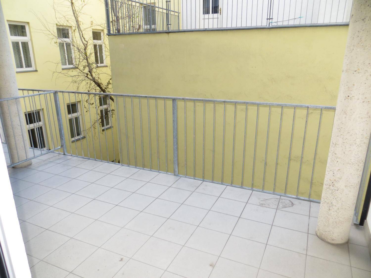 Gefliester Balkon mit Metallgeländer und Blick auf die umliegenden Gebäude im Innenhof.