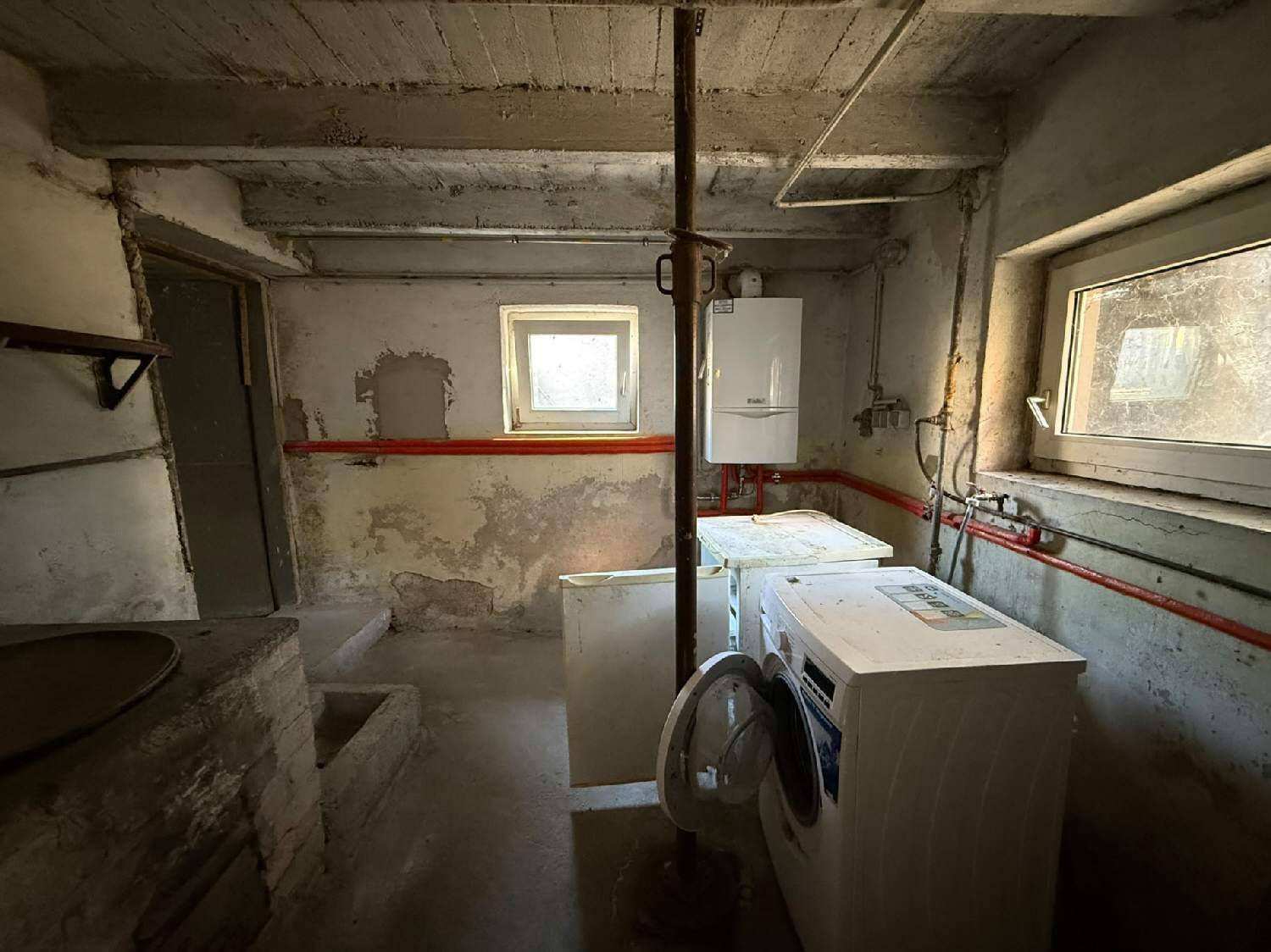 Waschküche im Keller mit Waschmaschine, Boiler und kleinen Fenstern.