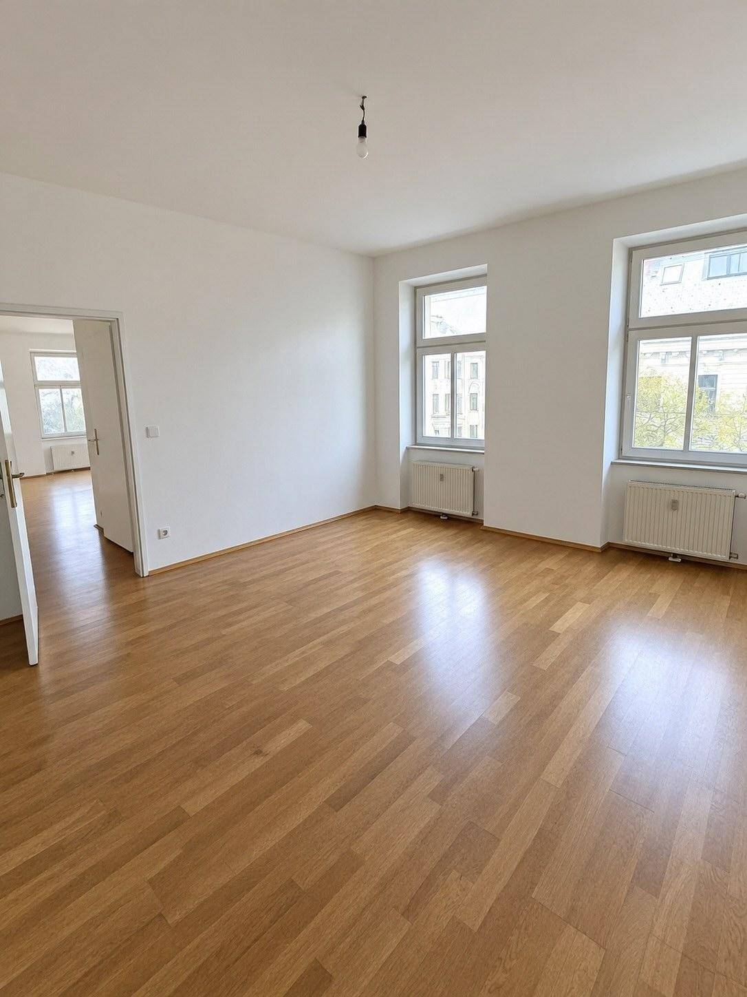 Großes, helles Zimmer mit Parkettboden und Zugang zu einem weiteren Raum, ideal für offenes Wohnen.