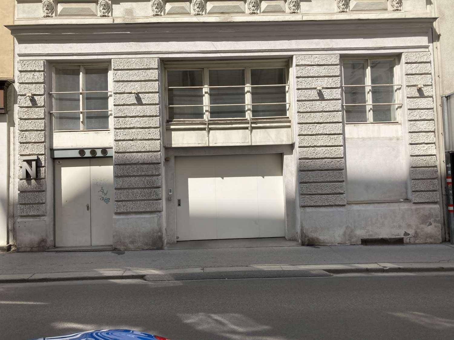 Erdgeschossfassade eines Gebäudes mit Garagentor und vergitterten Fenstern, robuste Steinverkleidung.
