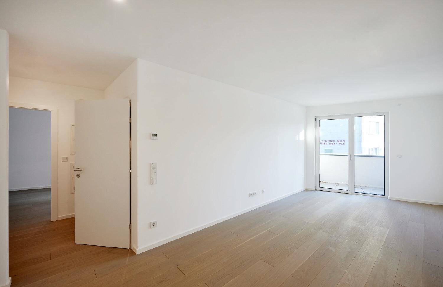 Helles Wohnzimmer mit Parkettboden und Zugang zu einem Balkon.