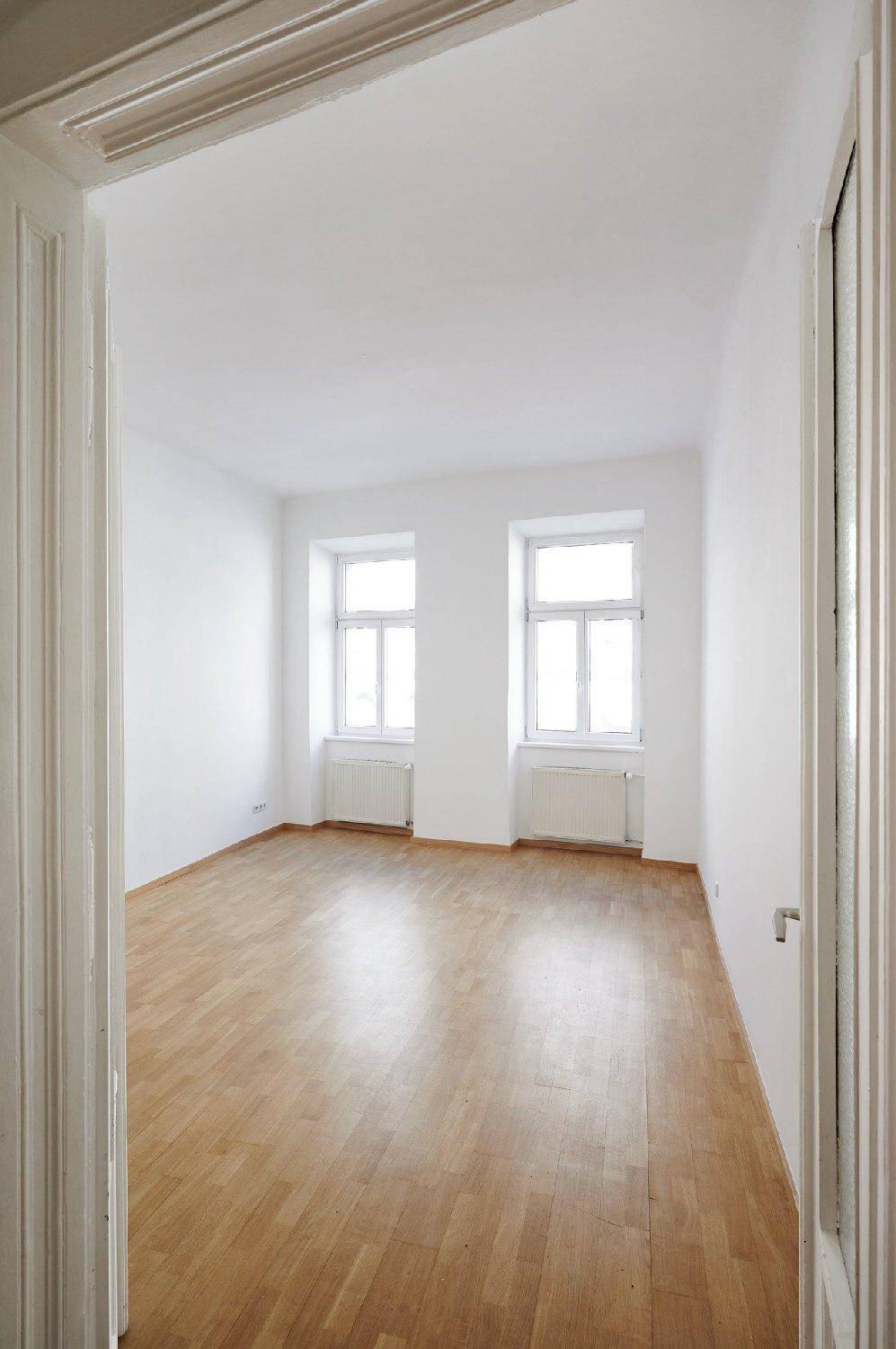 Geräumiges, helles Zimmer mit Parkettboden und zwei Fenstern, bereit für neue Bewohner.