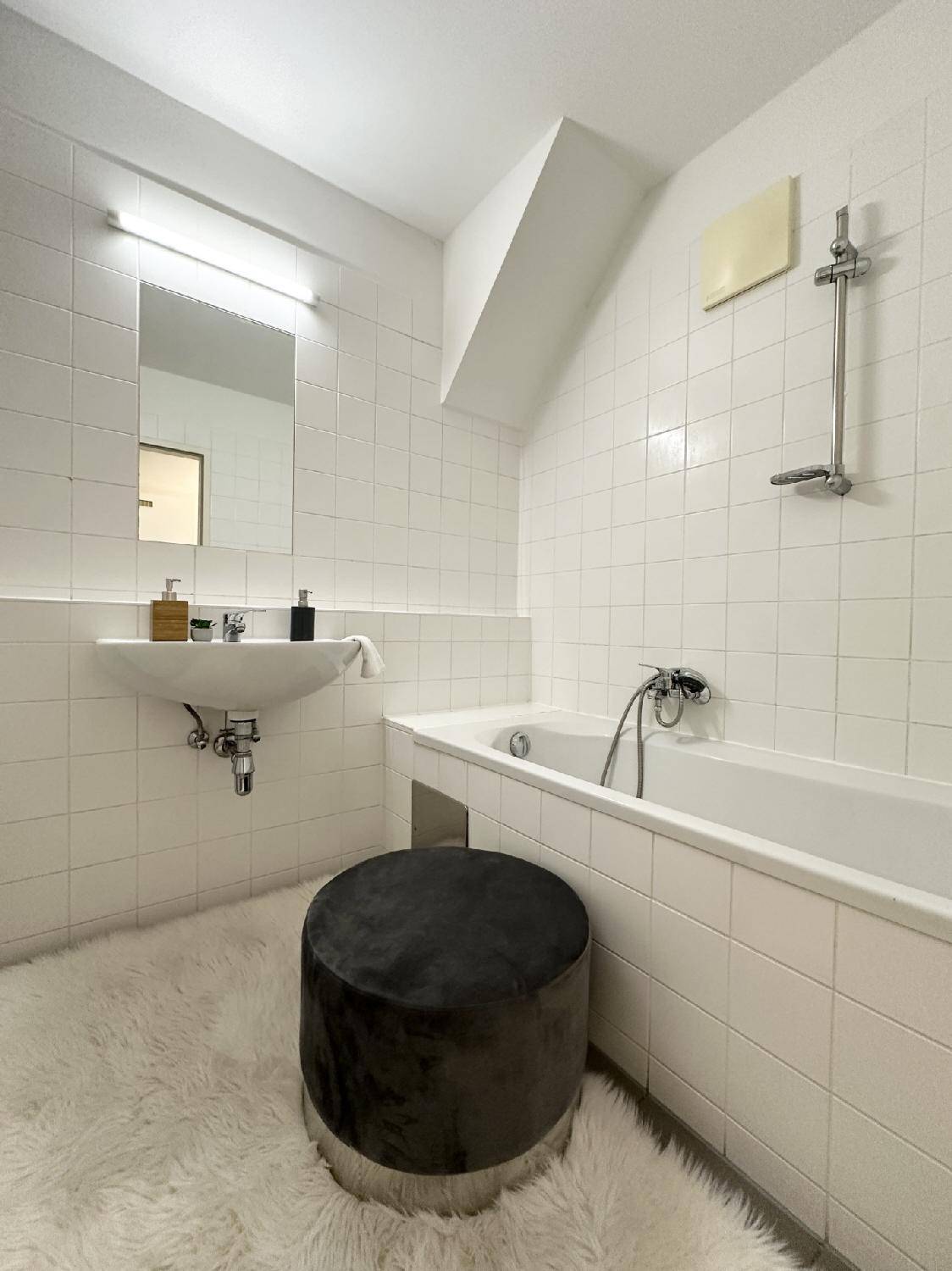Helles Badezimmer mit weißen Fliesen, Badewanne und einem einzelnen Waschbecken.