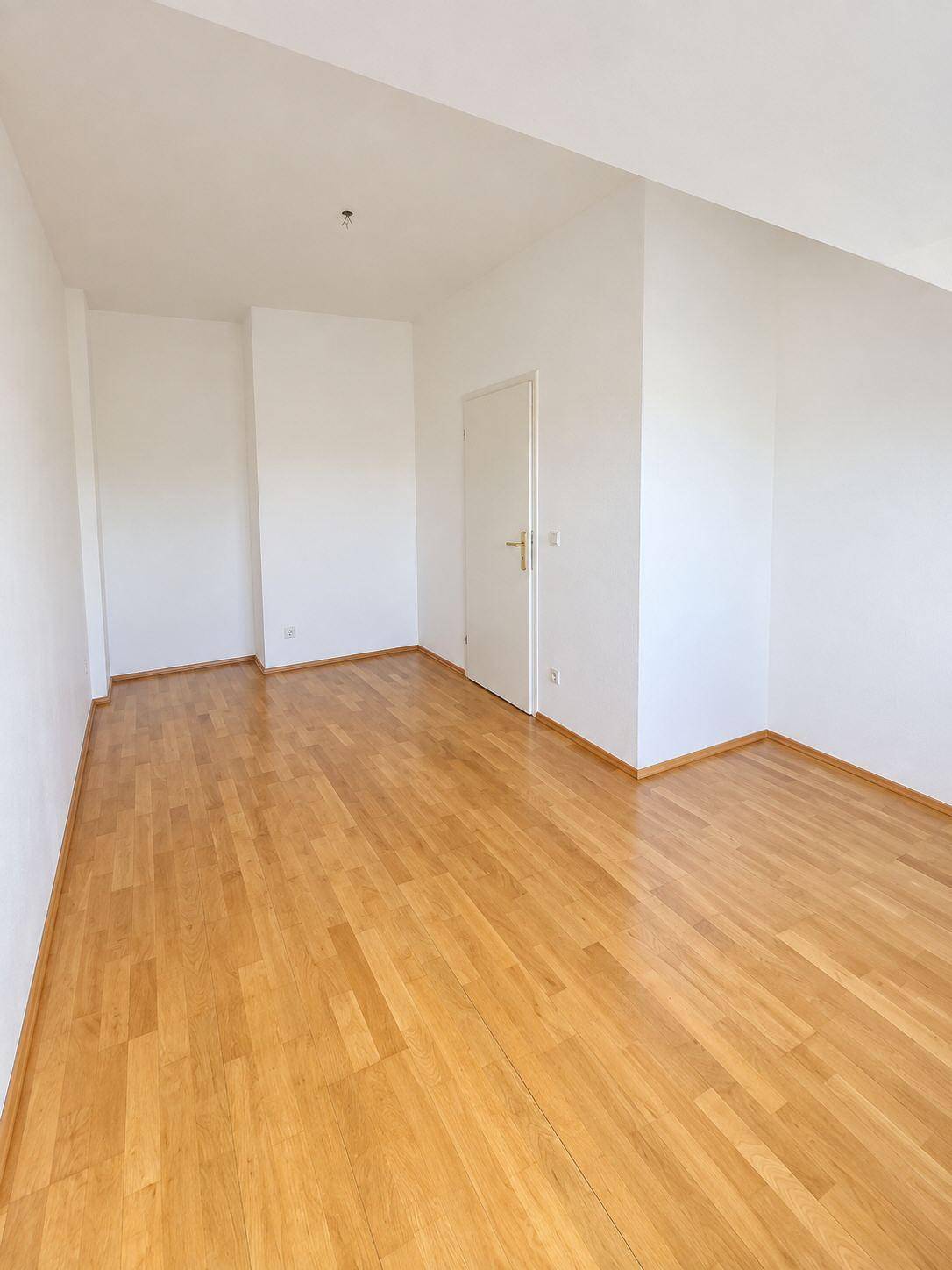 Leeres Zimmer mit hellem Holzfußboden und weißen Wänden, bereit zur individuellen Gestaltung.