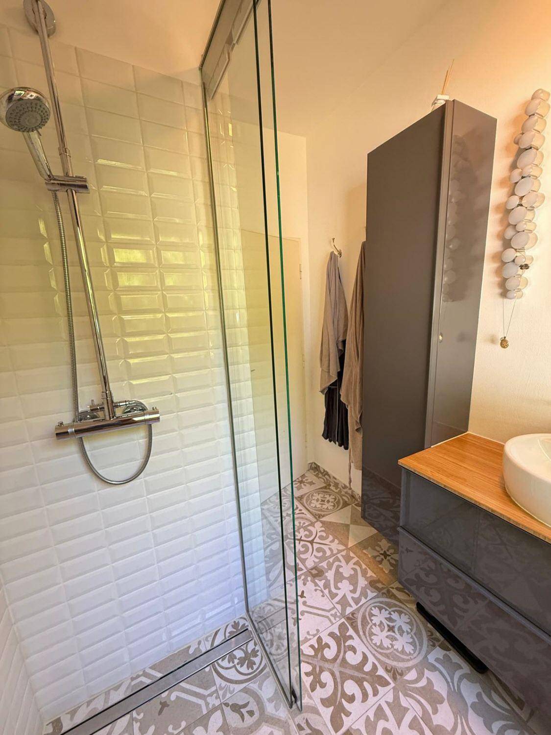 Duschbereich im modernen Badezimmer mit Glasabtrennung und gemustertem Fliesenboden.