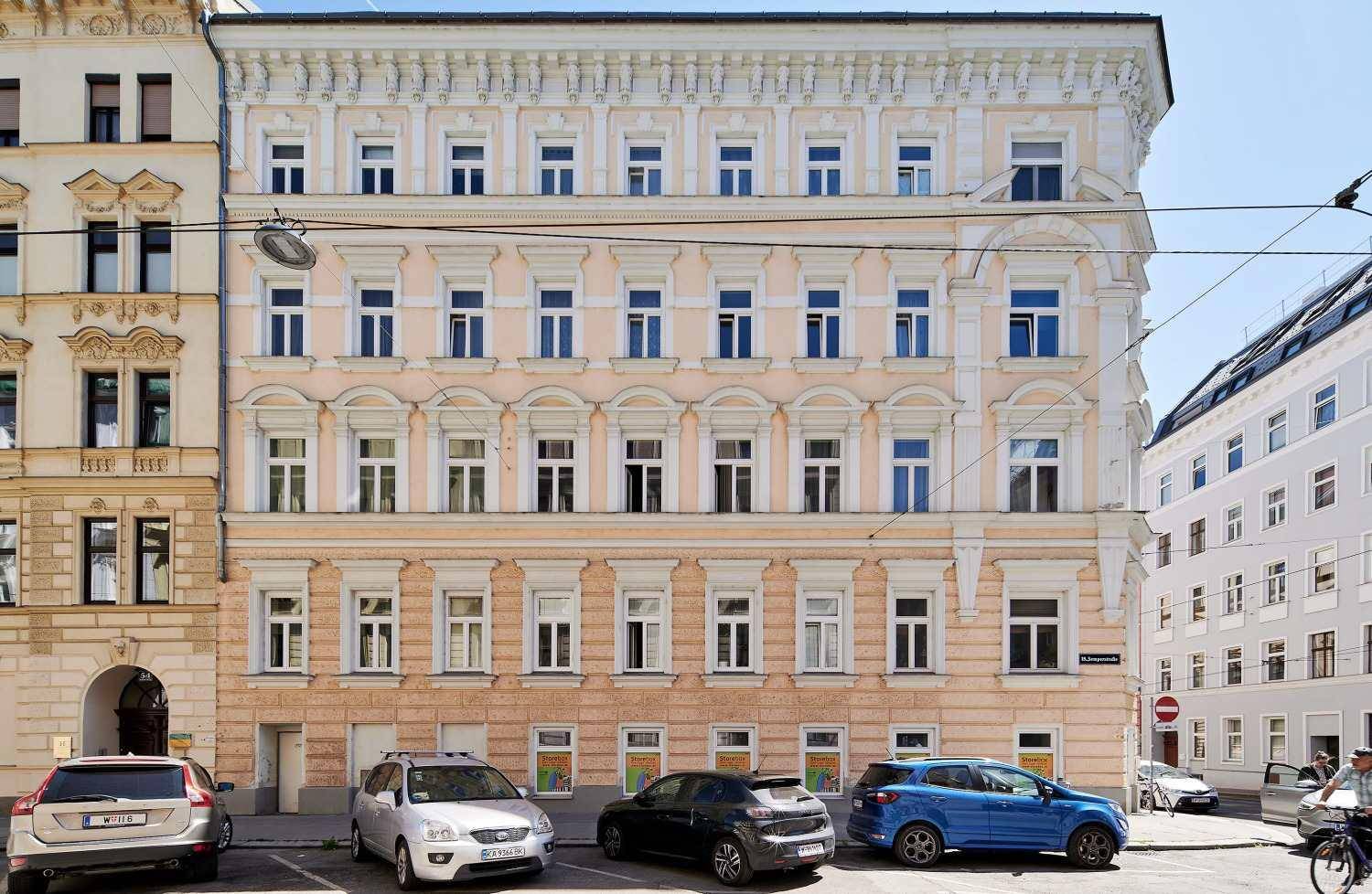 Historisches Wohngebäude mit eleganter Fassade, vielen Fenstern und geparkten Fahrzeugen davor.