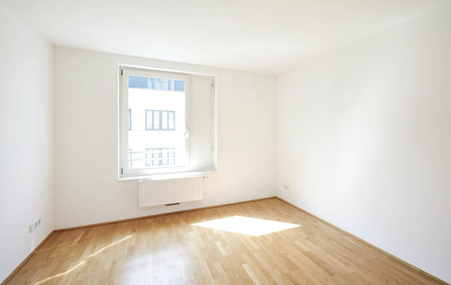 Freundliches Zimmer mit Parkettboden und einem Fenster, das den Raum mit Sonnenlicht erfüllt.