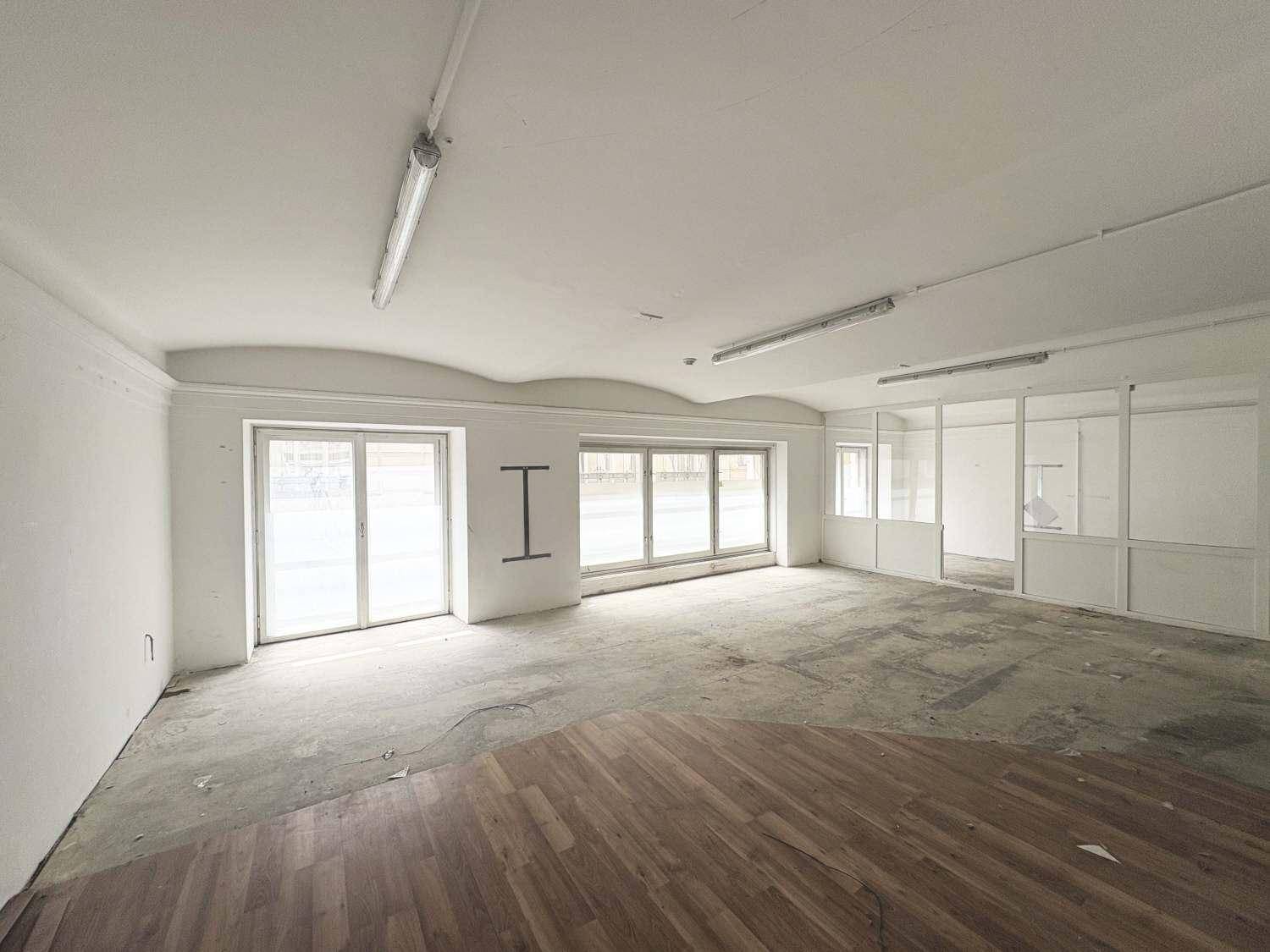 Geräumiger Gewerberaum mit großen Fenstern, Glasabtrennungen und einem Boden aus Beton und Holzparkett.