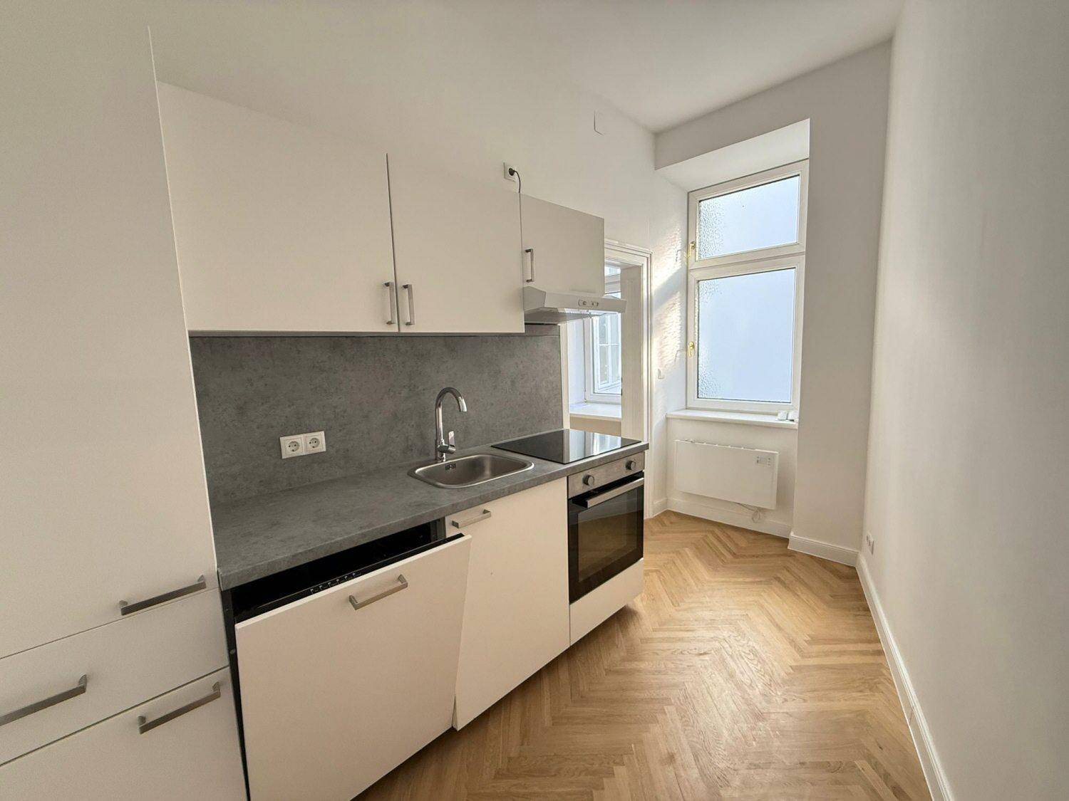 Moderne Küchenzeile mit weißen Schränken, integriertem Backofen und hellem Fischgrätparkett.