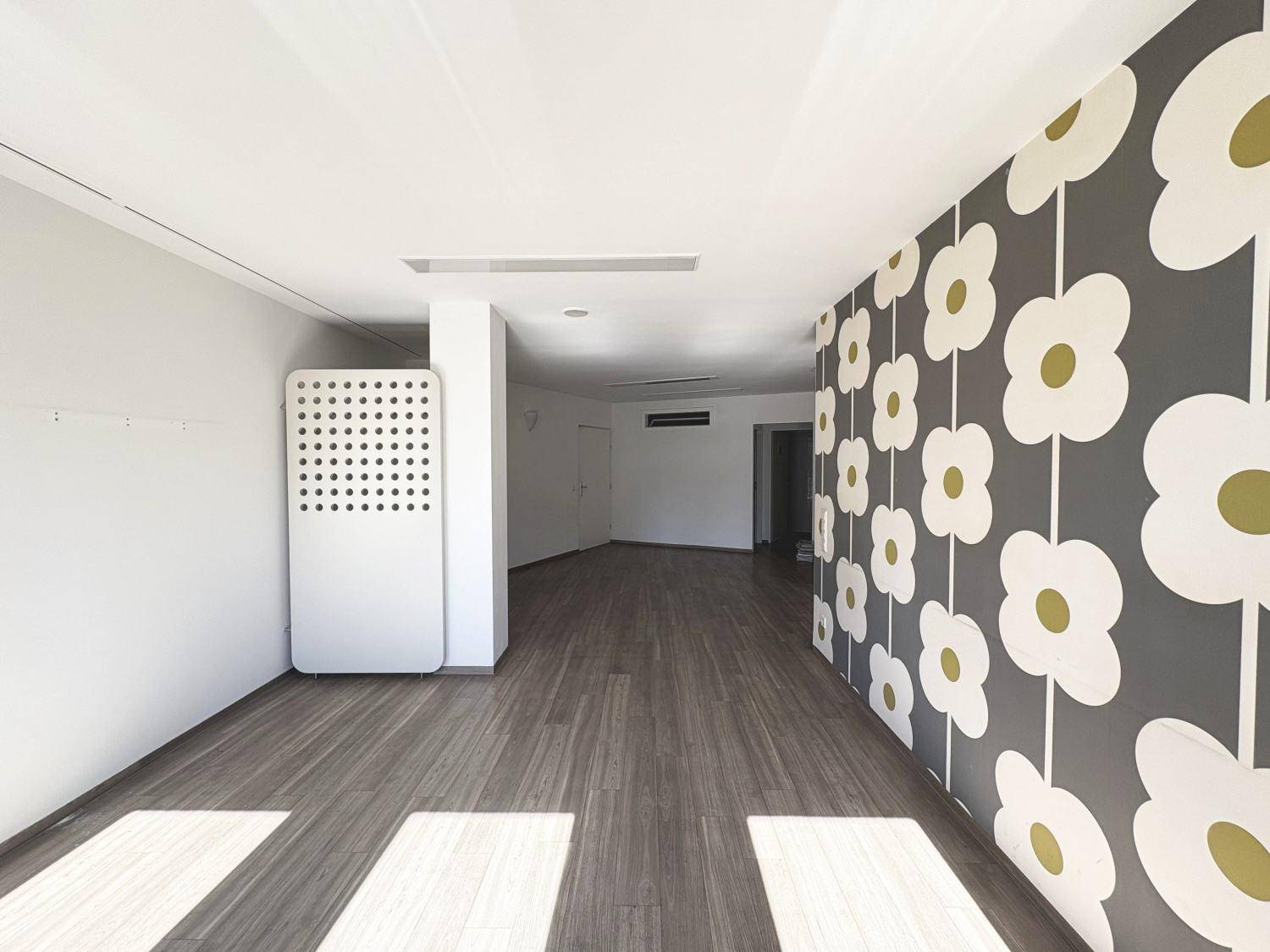 Langer, leerer Raum mit Holzboden und einer Wand, die mit einer auffälligen Blumentapete gestaltet ist.