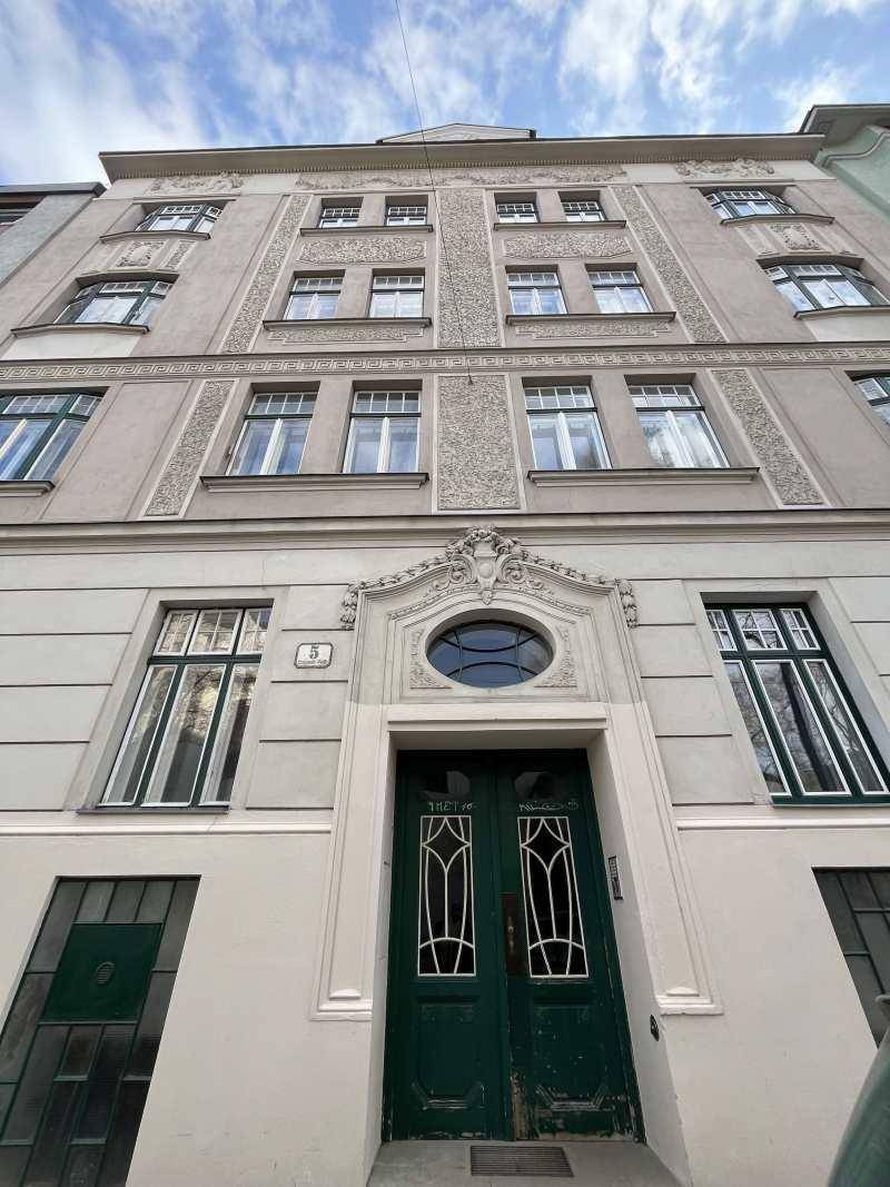 Detailansicht des verzierten Eingangsportals eines Altbaus mit grüner Doppeltür und Rundfenster.