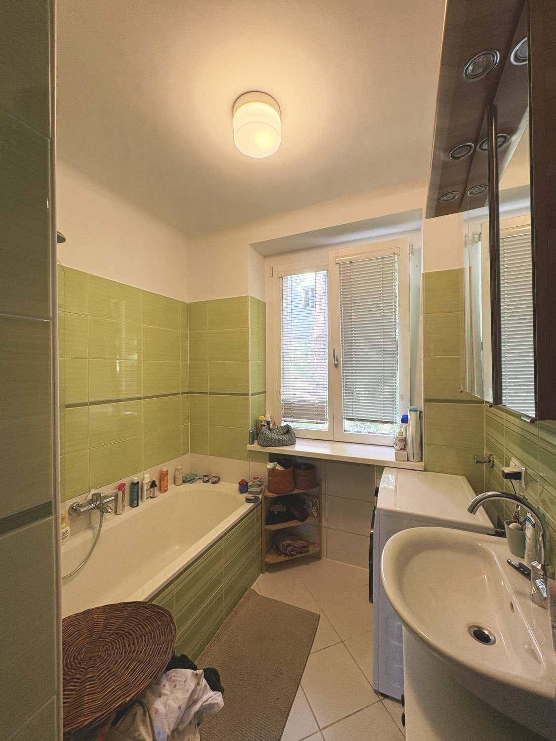 Badezimmer mit Badewanne, Waschbecken, Waschmaschine und grünen Wandfliesen.