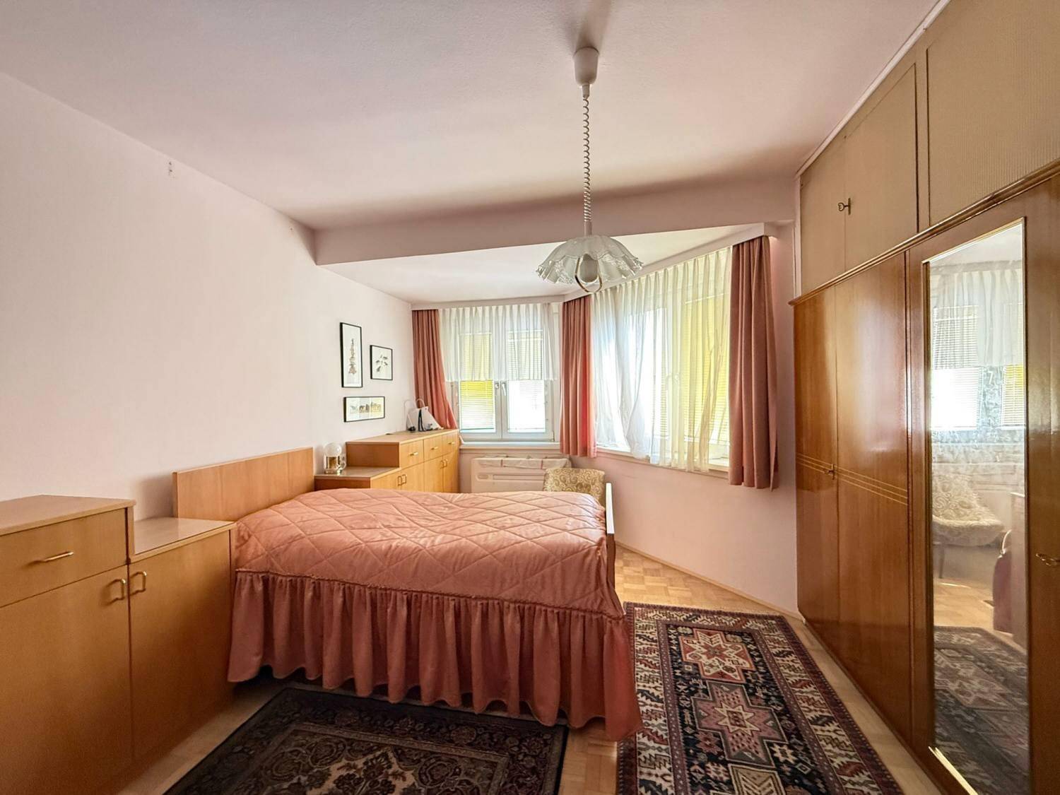 Schlafzimmer mit Einzelbett, Holzmöbeln und einem Erkerfenster, das viel Licht hereinlässt.