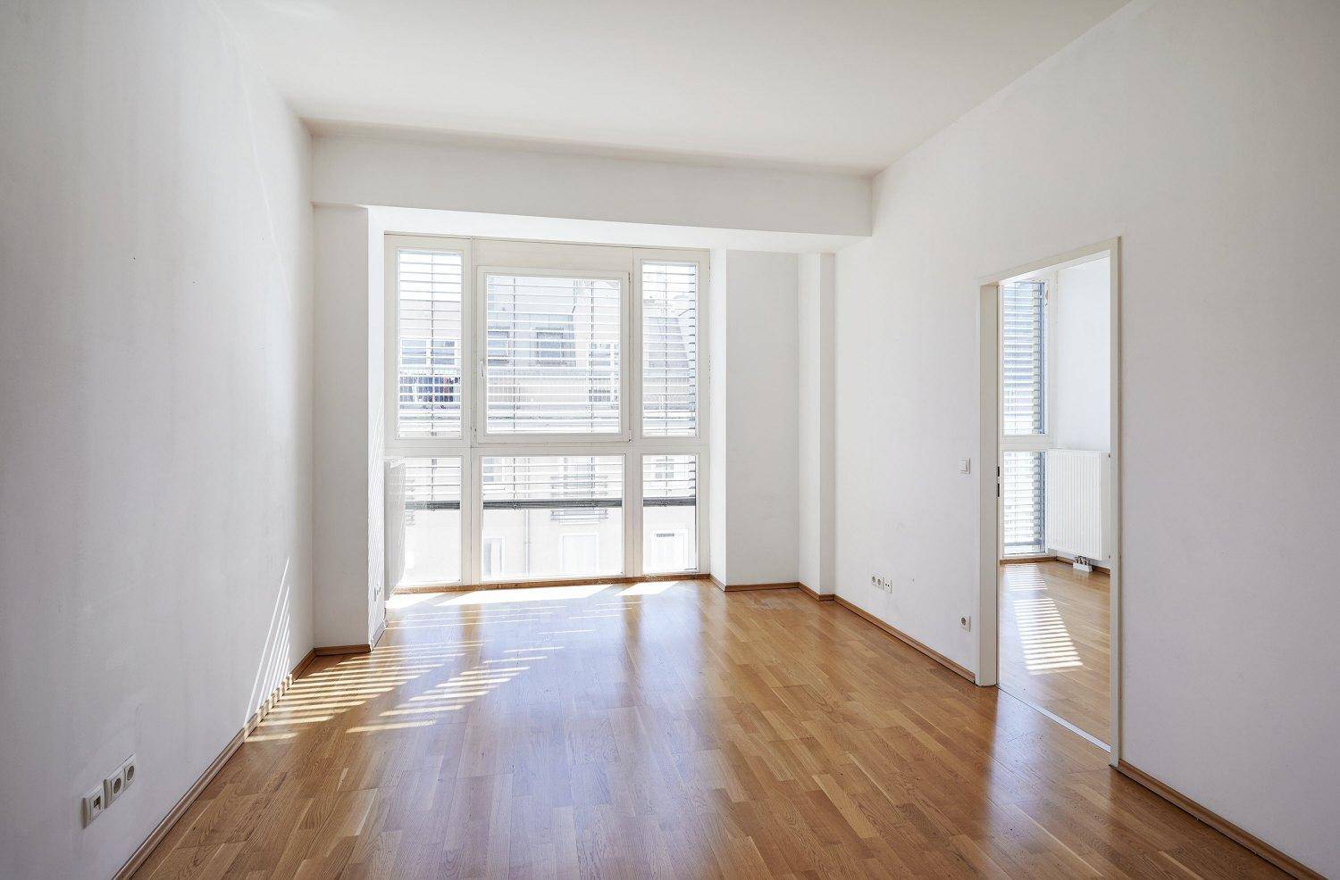 Lichtdurchfluteter Raum mit Holzboden und großen Fenstern, bereit für individuelle Gestaltung.