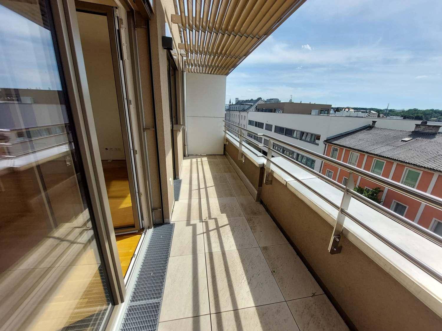 Langer Balkon mit Fliesenboden, Sonnenschutz und Blick auf die Stadt.