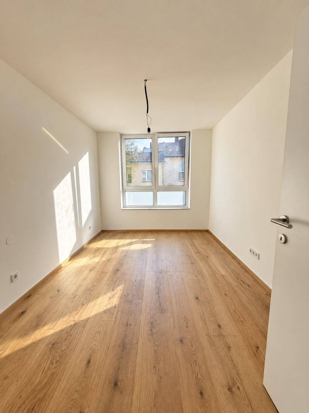 Helles Schlafzimmer mit Eichenparkettboden und großem Fenster, das viel Tageslicht hereinlässt.