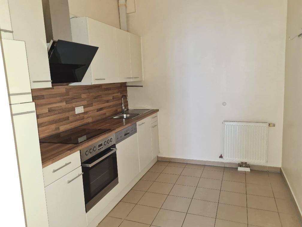 Moderne Einbauküche mit weißen Schränken, Holz-Arbeitsplatte, Induktionskochfeld und Fliesenboden.