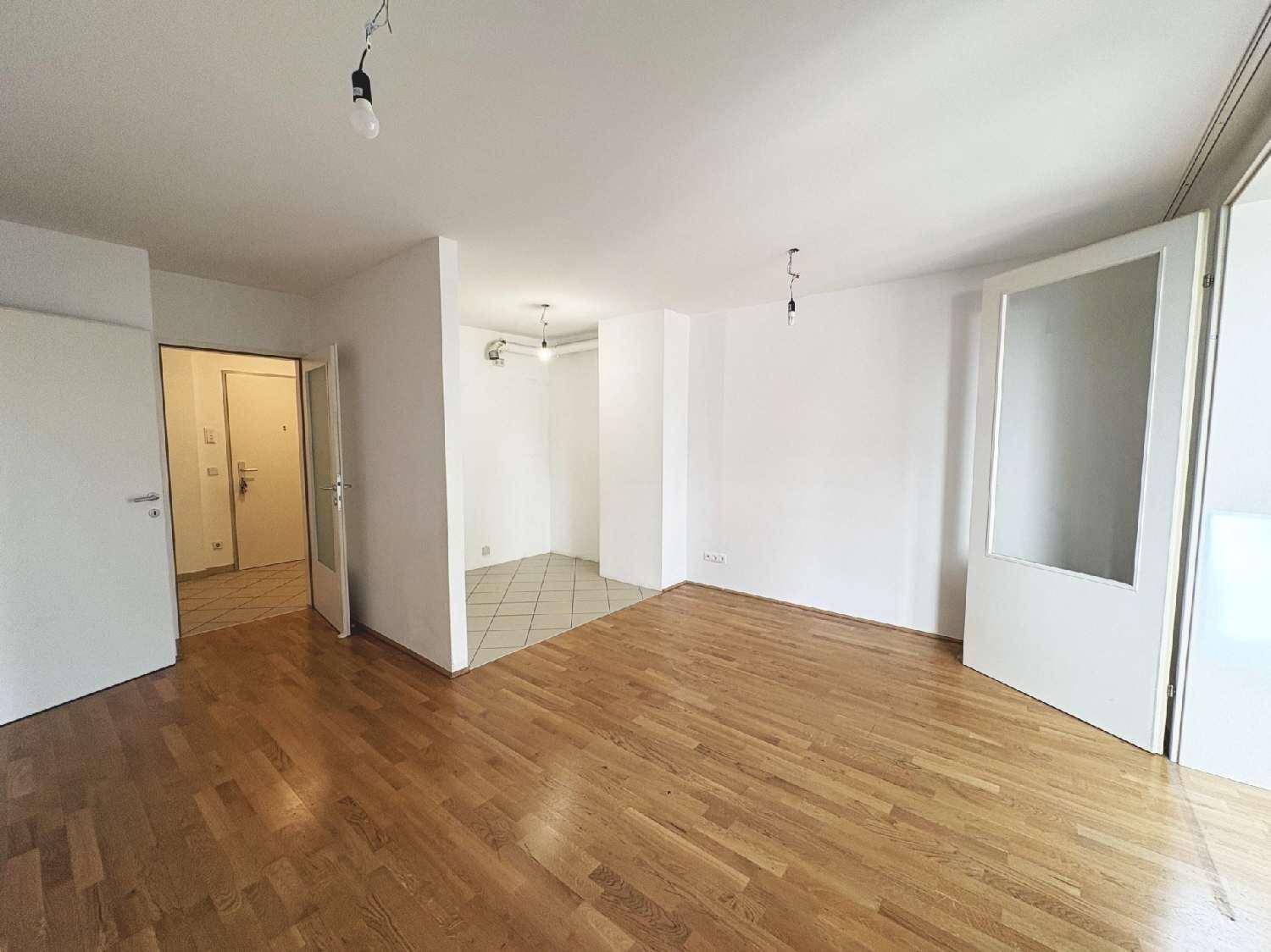 Heller, leerer Wohnbereich mit Parkettboden und einem gefliesten Abschnitt, der zu einem Flur führt.