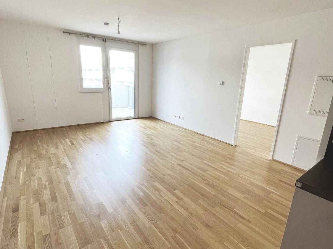 Lichtdurchfluteter Wohnraum mit Parkettboden und großem Fenster, das Zugang zu einem Balkon bietet.