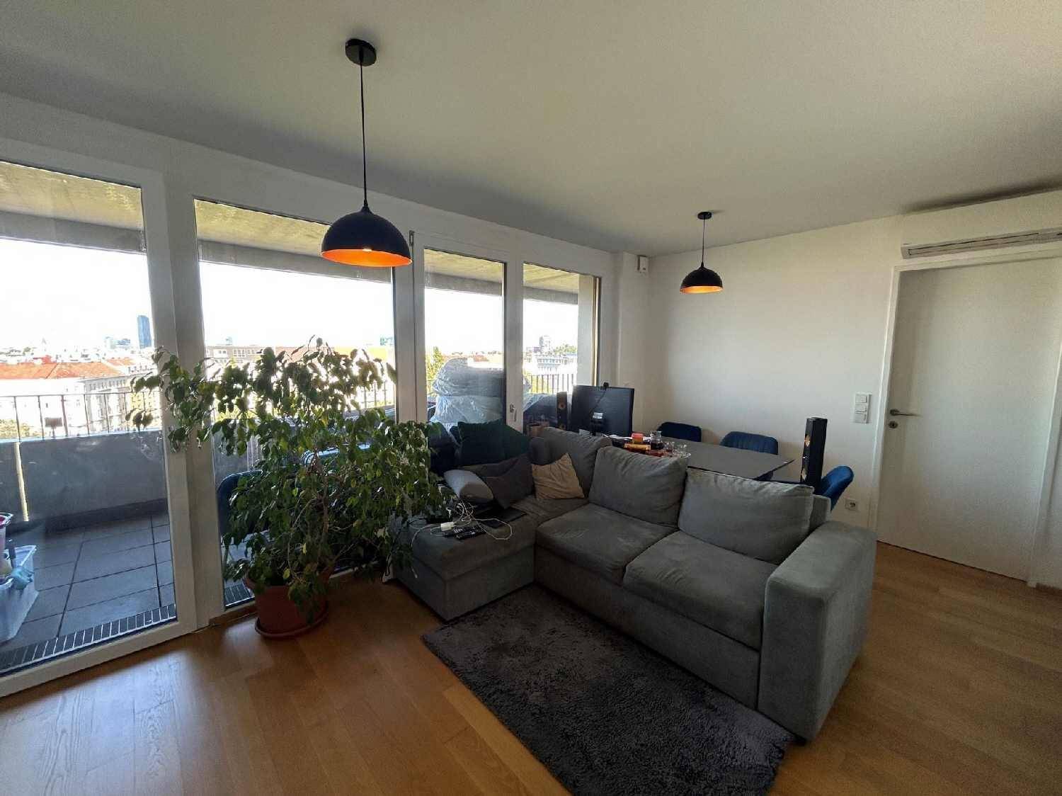 Helles Wohnzimmer mit gemütlichem Sofa, Holzboden und Zugang zum Balkon mit Stadtblick.