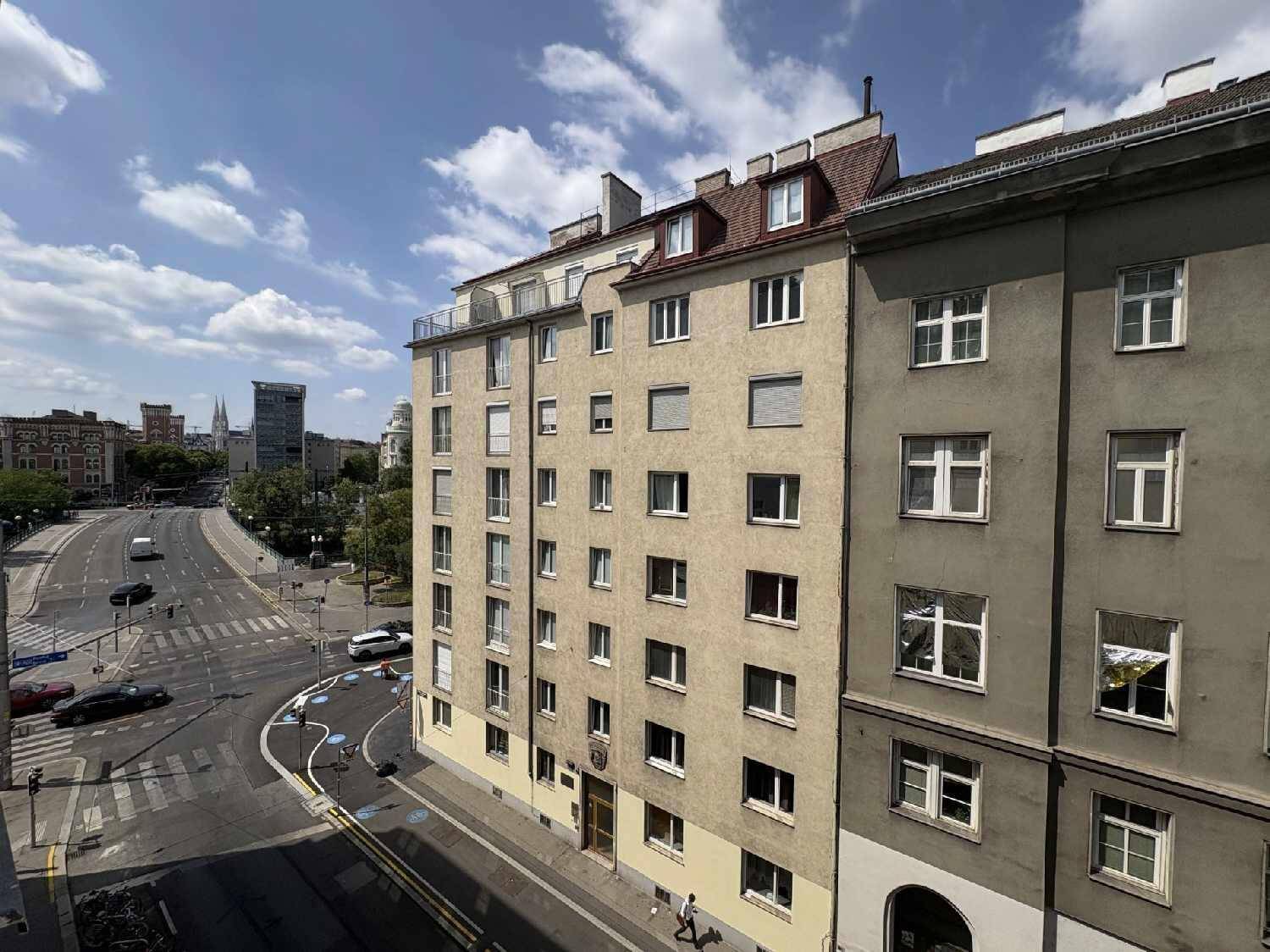 Mehrstöckiges Wohngebäude an einer belebten Straße unter blauem Himmel, mit Stadtblick.