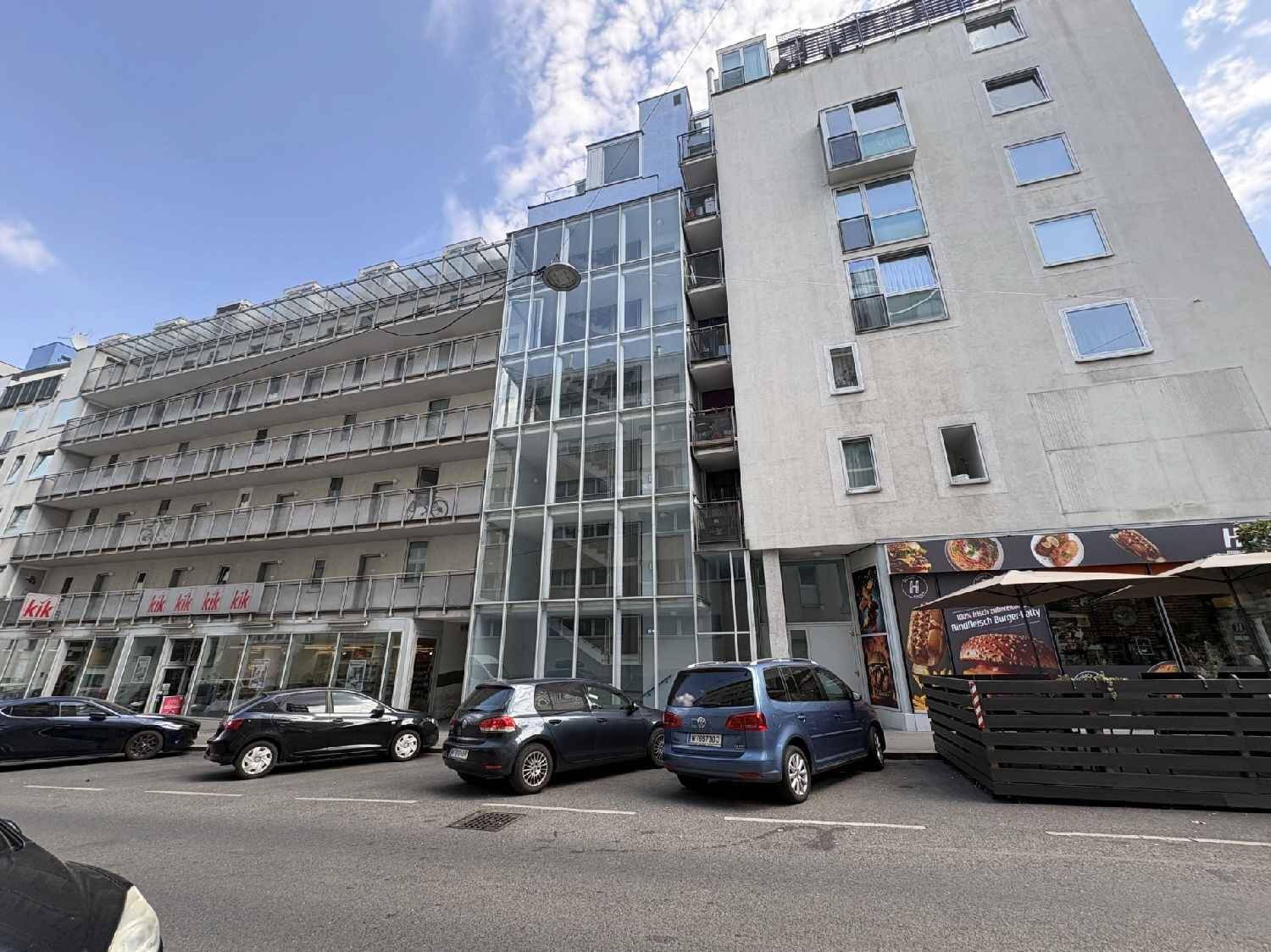 Moderne Wohngebäude-Fassade mit großen Glasfronten und einem außenliegenden Aufzug.