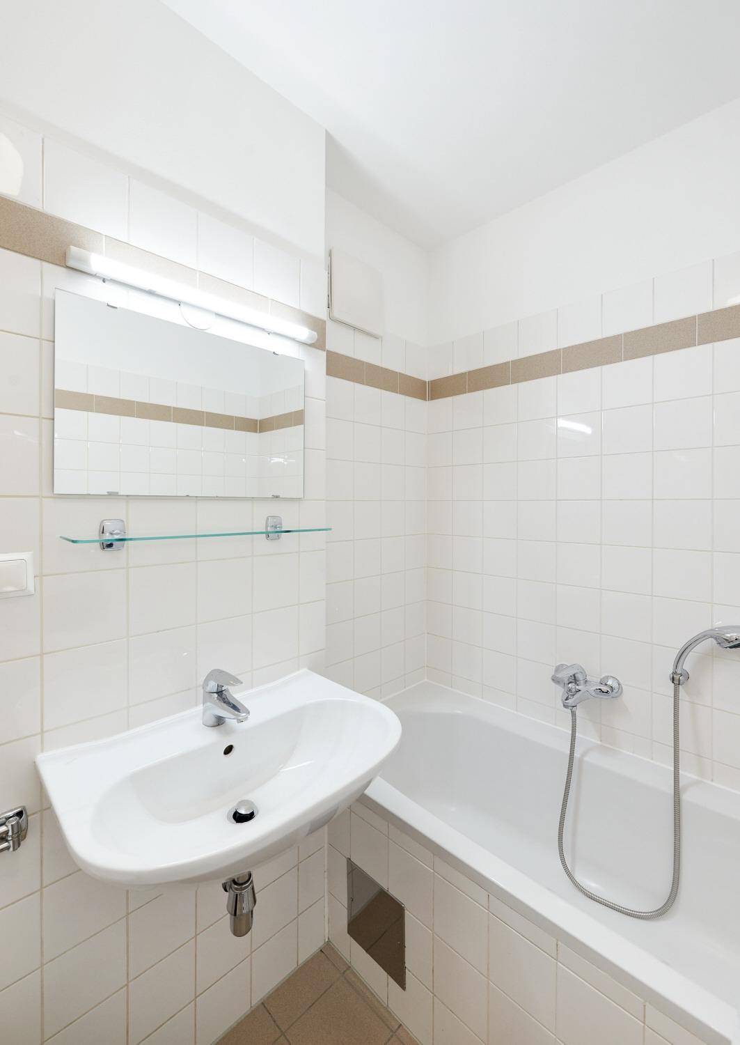 Detailaufnahme des Badezimmers mit Waschbecken, Spiegel und Badewanne mit Duschfunktion.