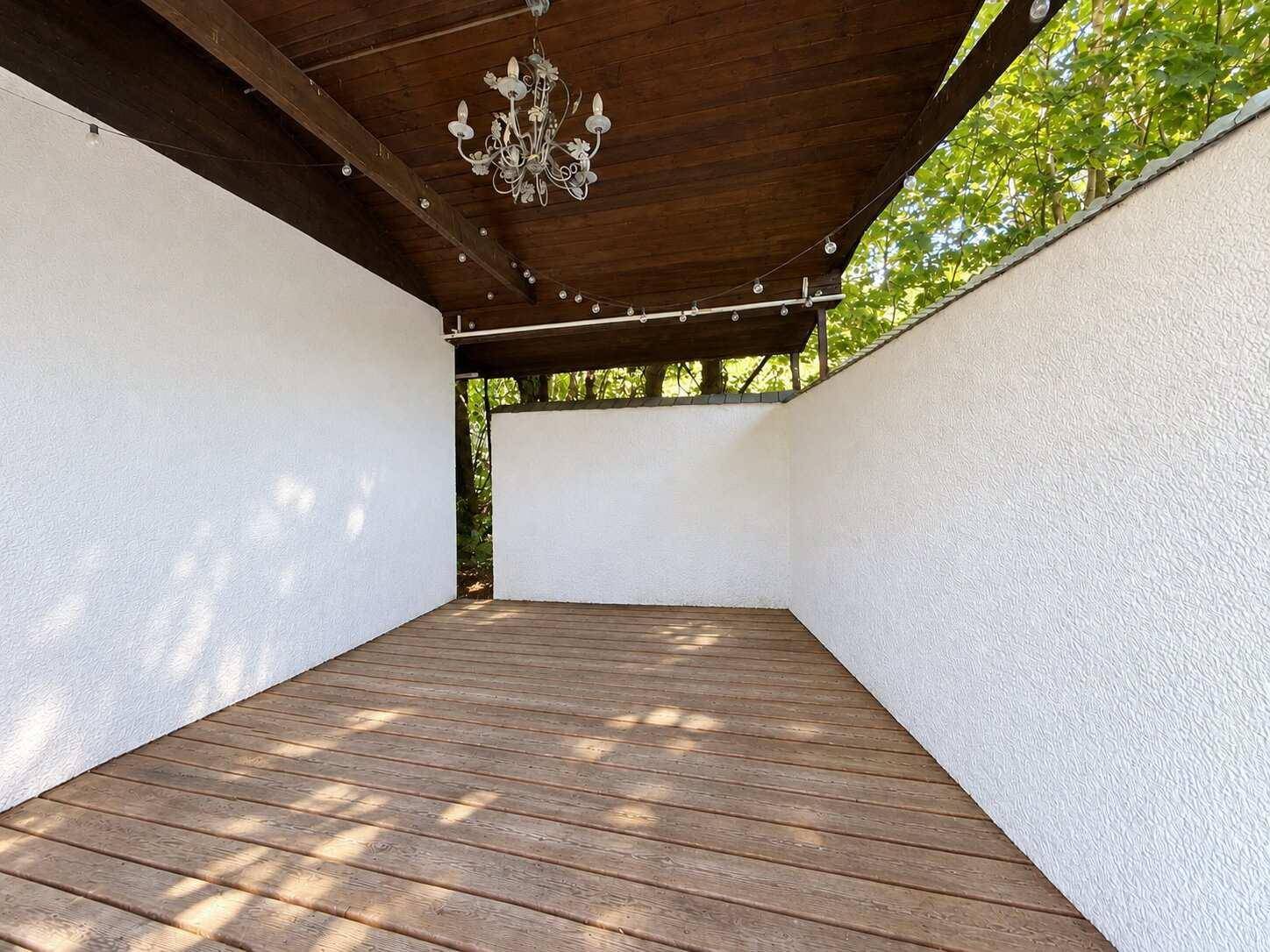 Überdachte Holzterrasse mit weiß gestrichenen Wänden und einer eleganten Deckenleuchte.