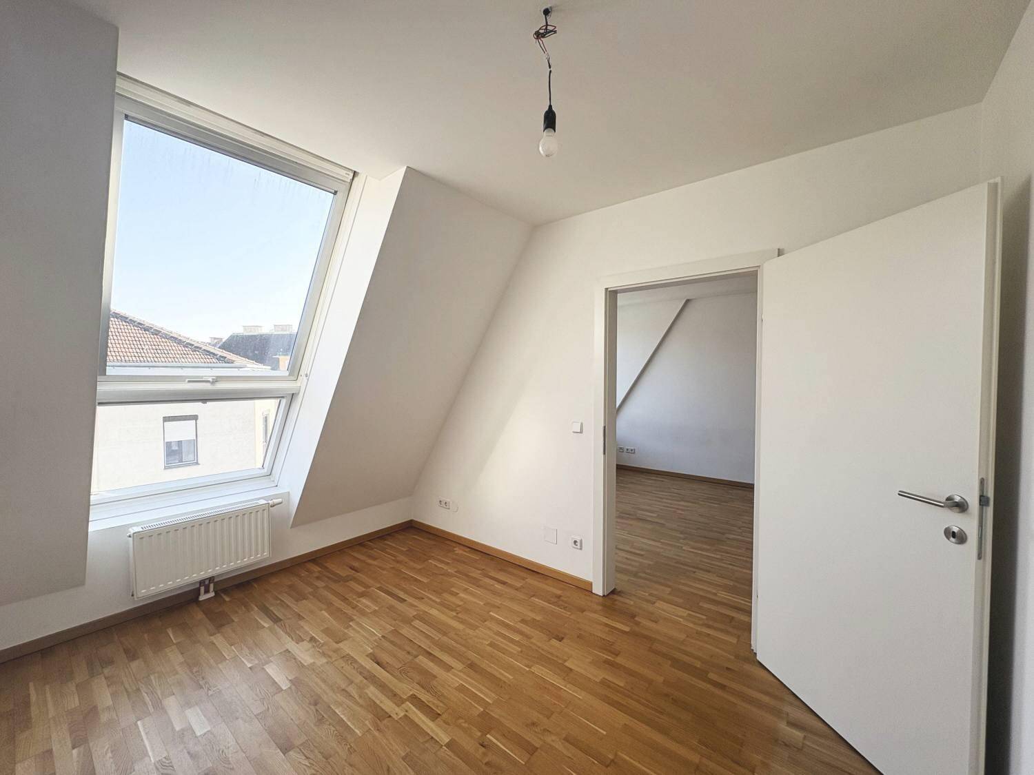 Helles Schlafzimmer mit Parkettboden, Dachschräge und großem Fenster für viel Tageslicht.