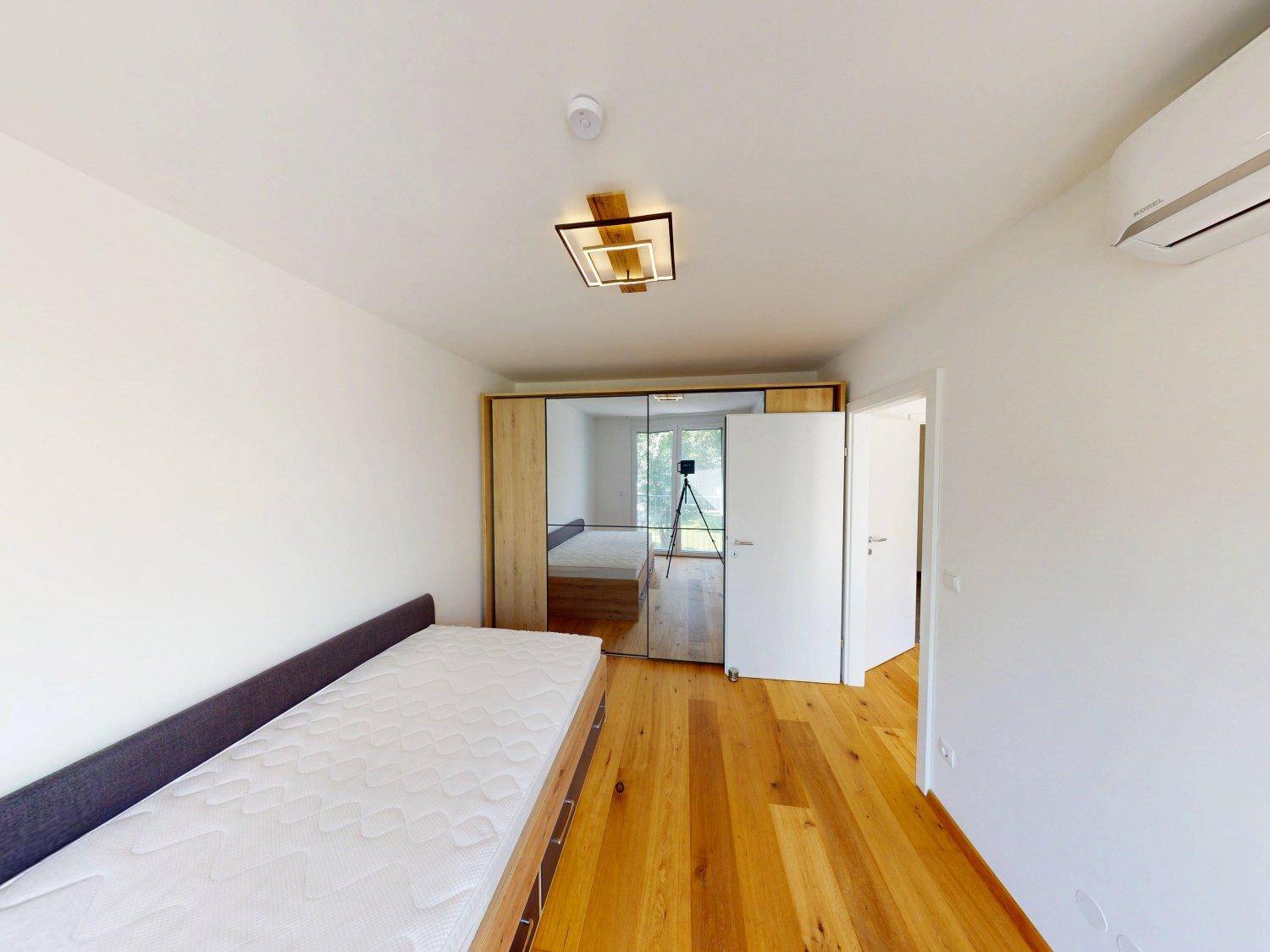 Schlafzimmer mit Holzboden, Spiegelschrank und Blick in den angrenzenden Raum.