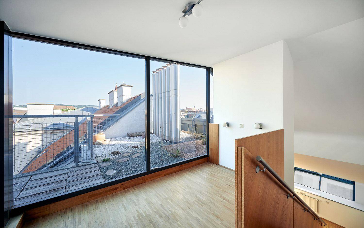 Heller Raum mit großen Fenstern und Blick auf die Dachterrasse und die Stadt.