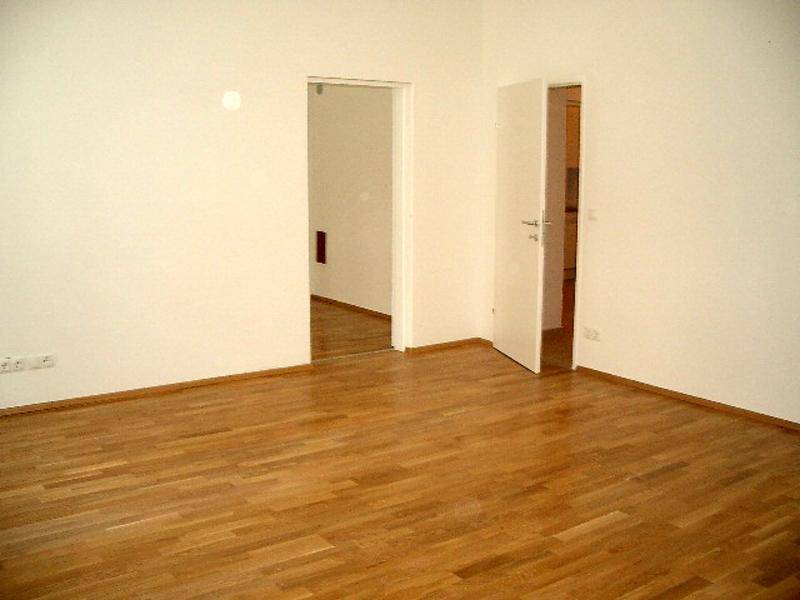 Leerer Raum mit hellem Parkettboden und zwei offenen Türen zu angrenzenden Zimmern.