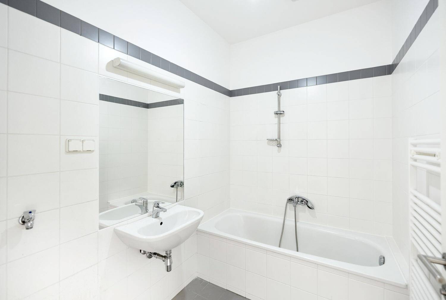 Modernes Badezimmer mit weißen Fliesen, Badewanne und einem einzelnen Waschbecken.