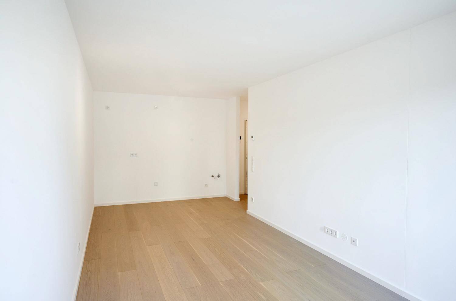 Geräumiger, leerer Raum mit hellem Parkettboden und weißen Wänden.