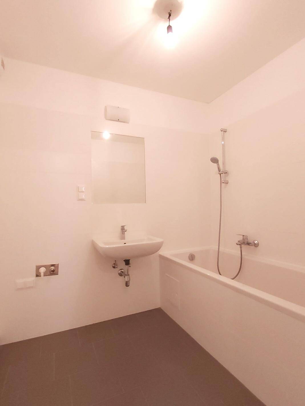 Modernes Badezimmer mit Badewanne, Waschbecken und Spiegel, ausgestattet mit grauen Fliesen.