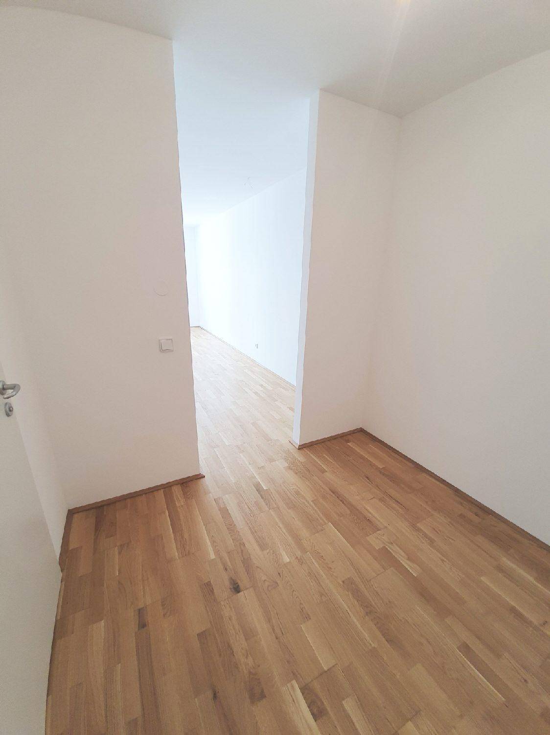 Heller Flur mit Parkettboden und weißen Wänden, der zu weiteren Räumen führt.