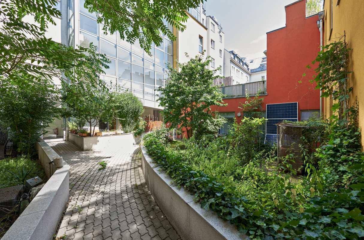 Gepflegter Innenhof mit üppiger Vegetation, einem gepflasterten Weg und modernen Gebäudefassaden.