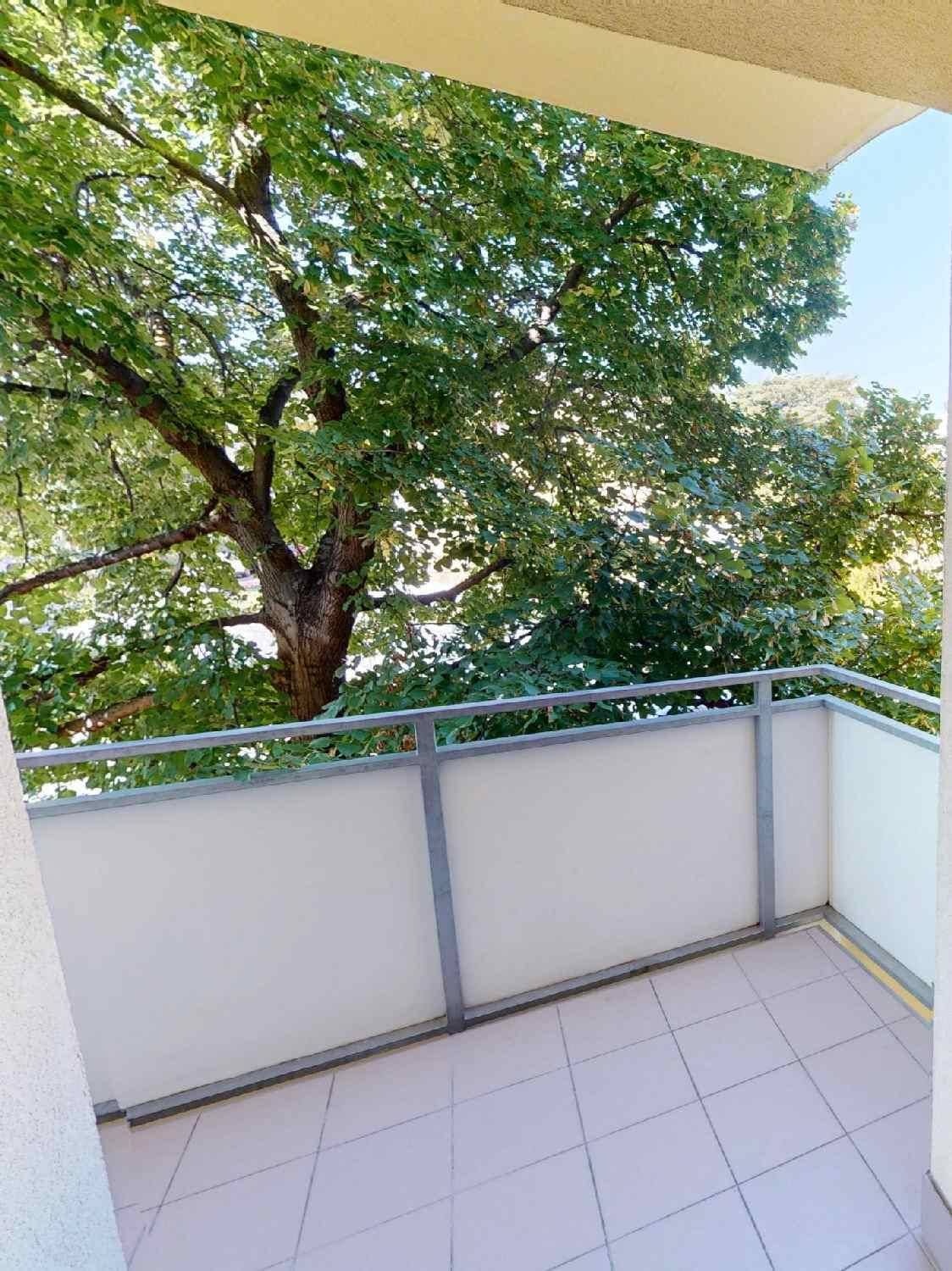 Heller Balkon mit Fliesenboden und Blick ins Grüne, umgeben von Bäumen.
